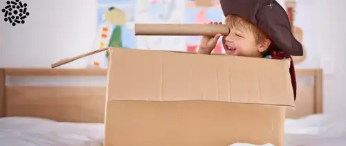Criança pequena cria sua brincadeira de pirata, usando caixa de papelão e sucata