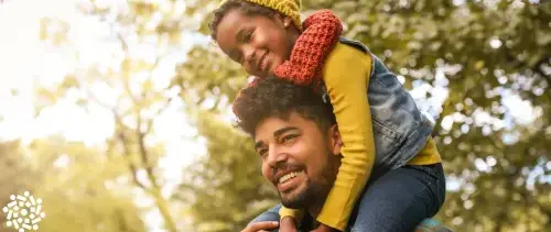 Pai carrega filha nos ombros: brincadeira ao ar livre nas férias