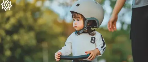 Criança pequena de capacete anda de triciclo ao lado de um adulto. Conheça os benefícios da prática e cuidados necessários